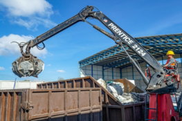 Crane with grapple loading debris into a dumpster